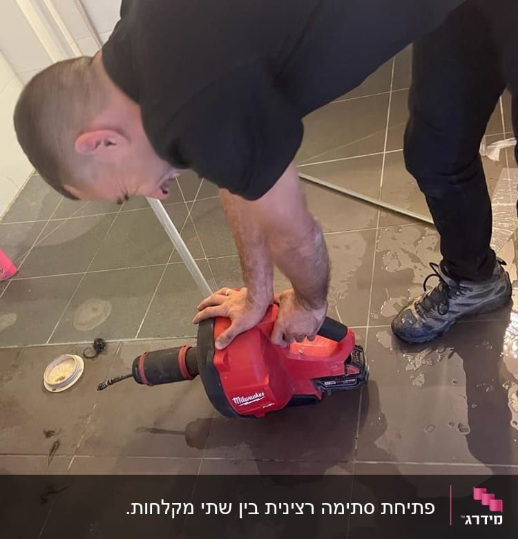 אדם משתמש במקדחה אדומה על רצפת חדר אמבטיה רטובה